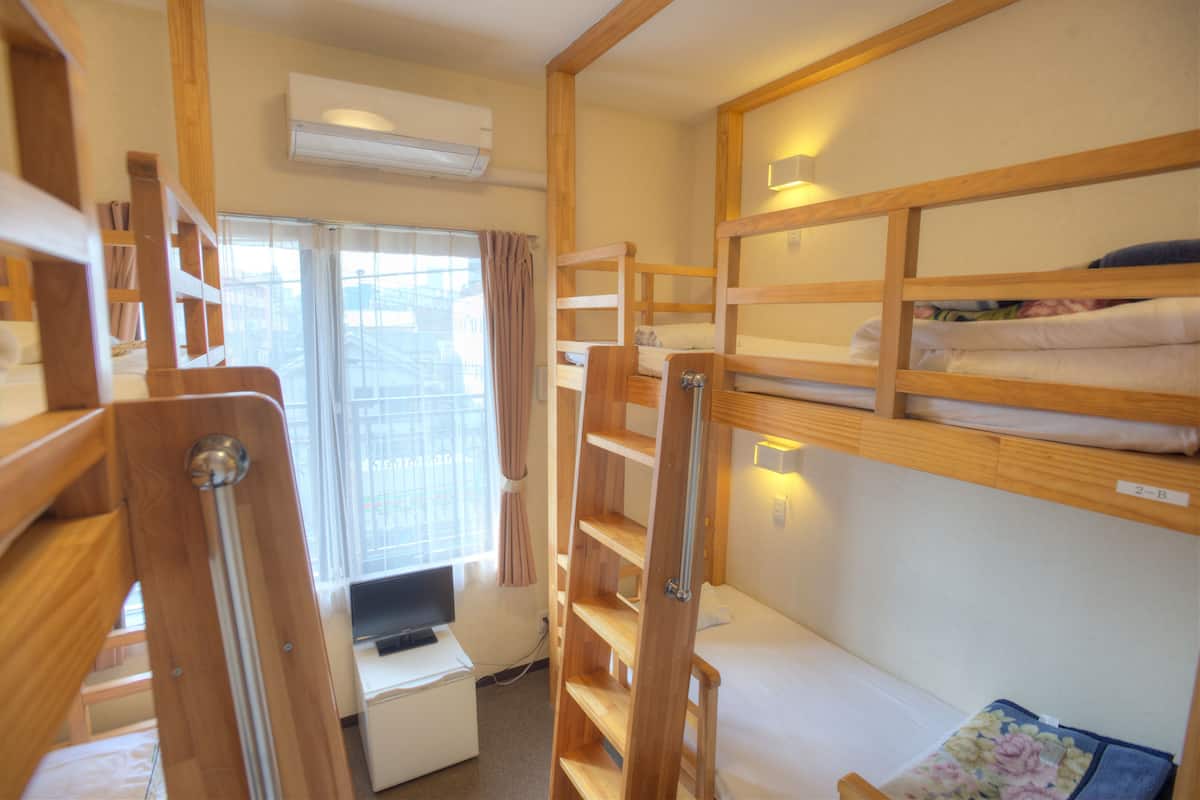Ein kleines Zimmer mit Etagenbetten, einem Schreibtisch mit Computer und einem Fenster mit Vorhängen.