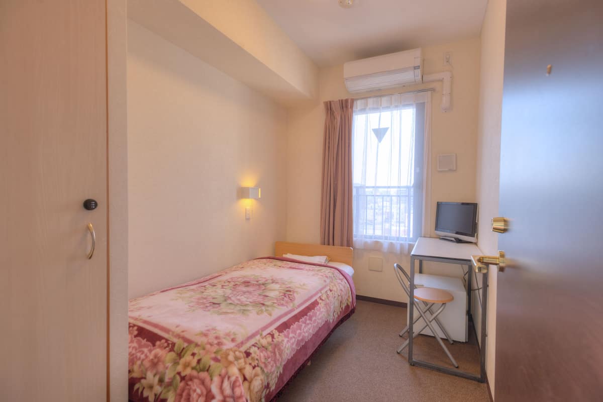 Ein kleines Schlafzimmer mit Bett, Schreibtisch, Stuhl und Fernseher.