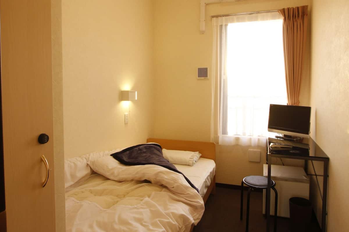 Ein Hotelzimmer mit Bett, Schreibtisch mit Computer, Fenster mit Vorhängen und einer Klimaanlage.