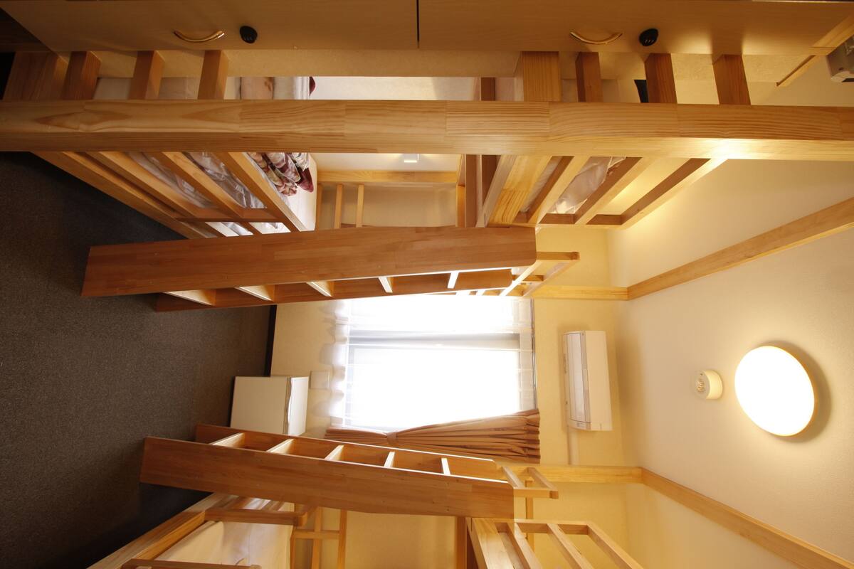 Ein Zimmer mit schrägen Wänden und Holzbalken, einem Bett, einem Nachttisch und einer Wandleuchte.