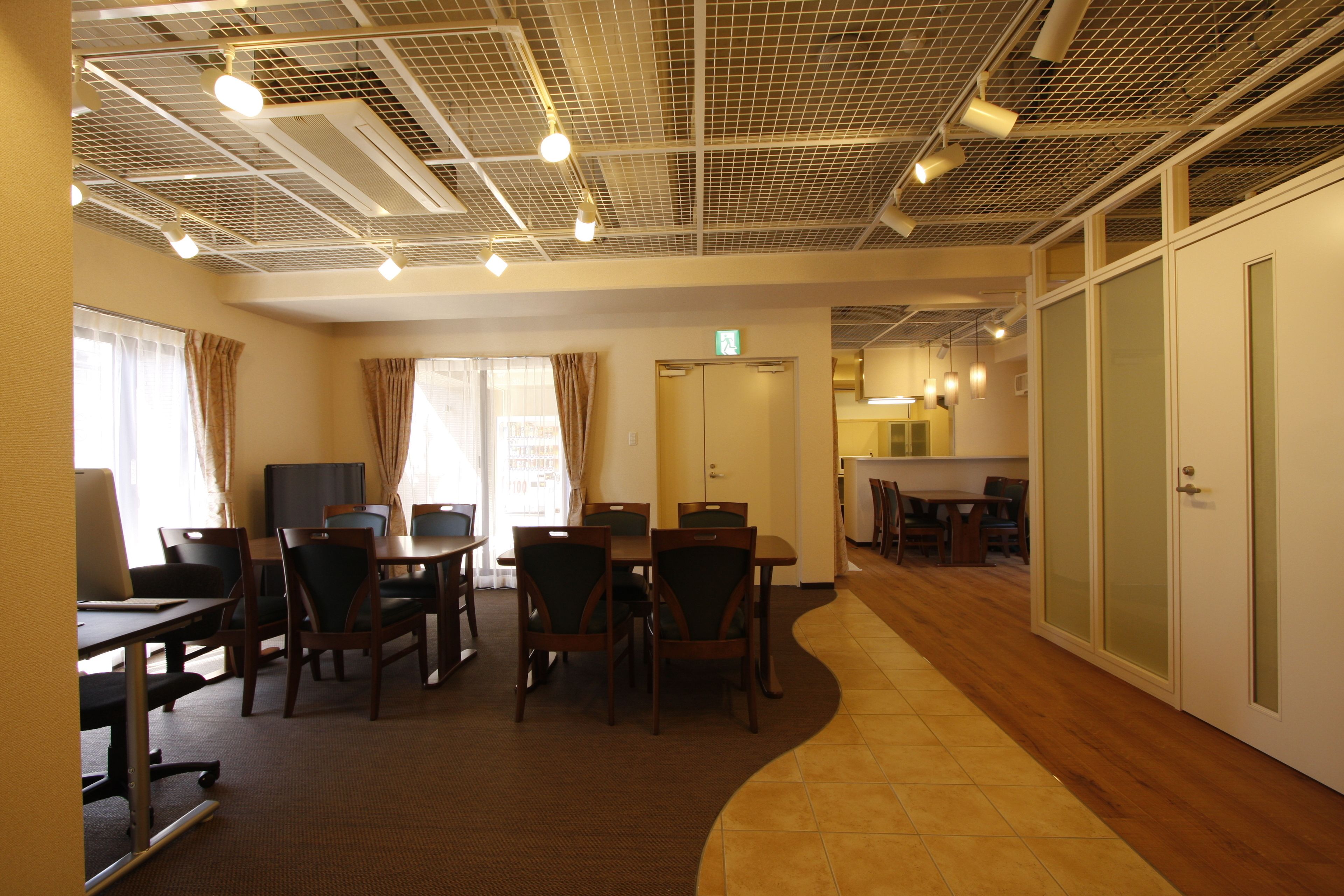 A conference room with a long table, chairs, a television, and a kitchen area in the background.