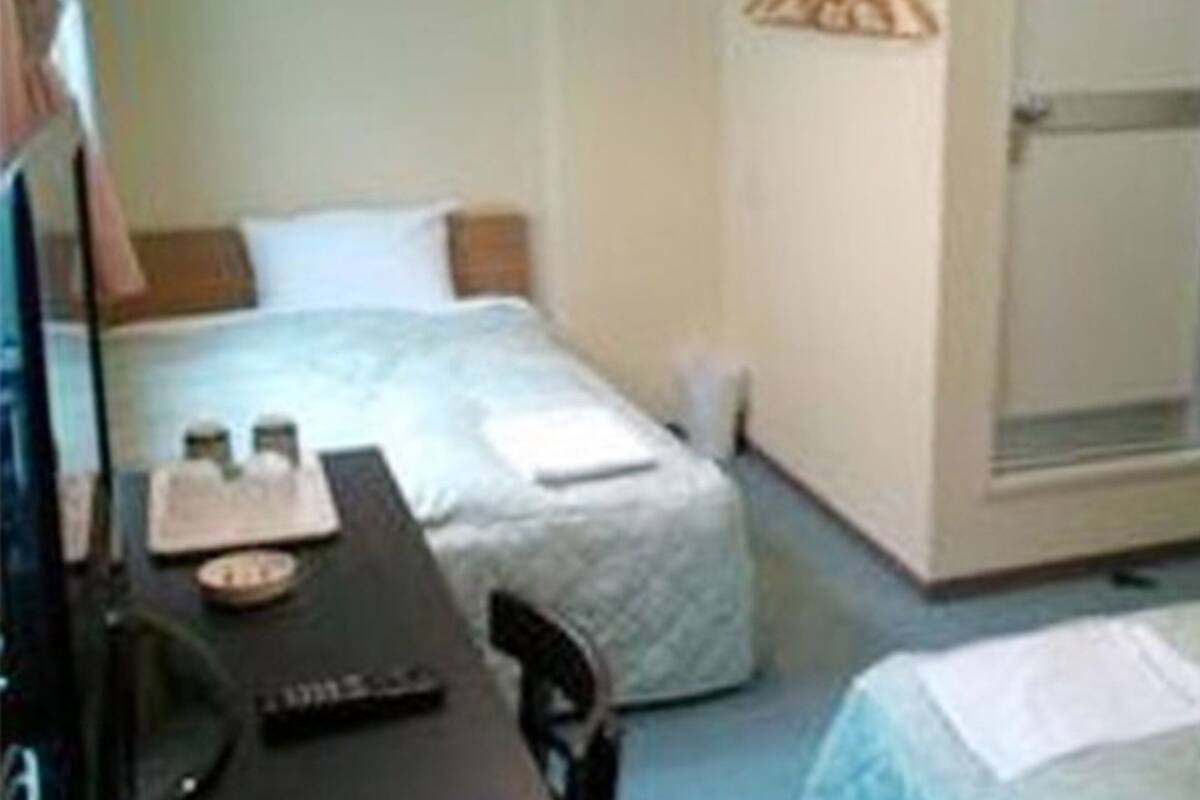 Quarto pequeno e simples com duas camas, uma escrivaninha e um guarda-roupa.