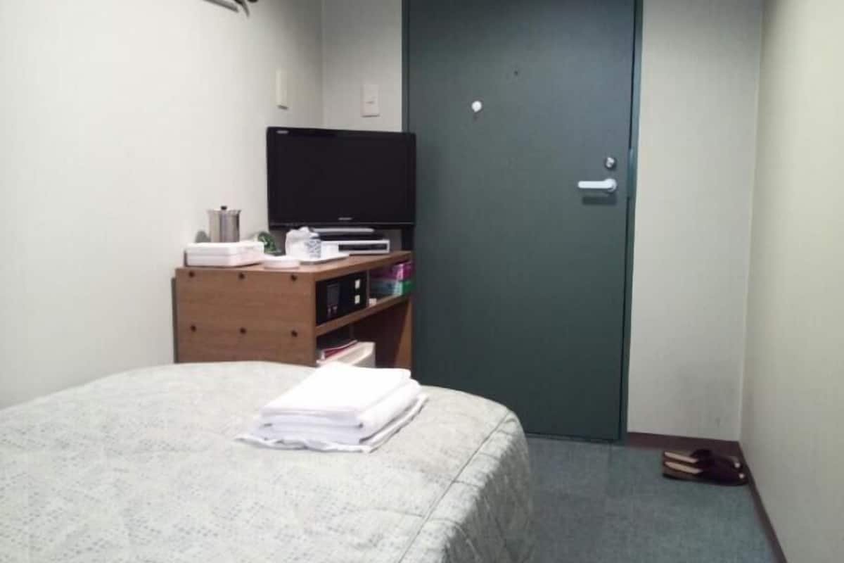 Una habitación pequeña con una cama, un aparador de madera, un televisor y una puerta.