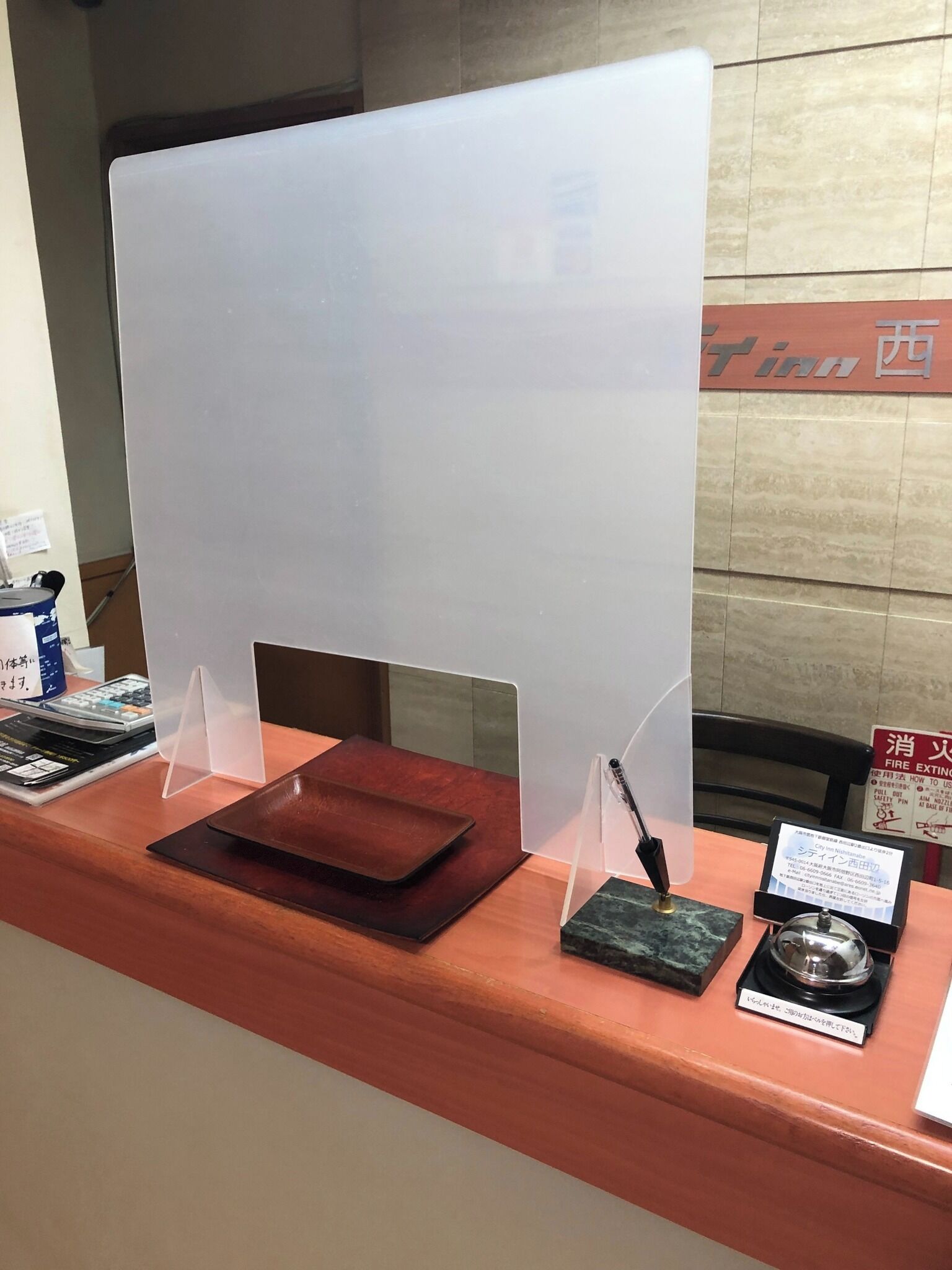 Una mesa de recepción con un monitor de computadora, un portalápices, una pequeña caja y un extintor.