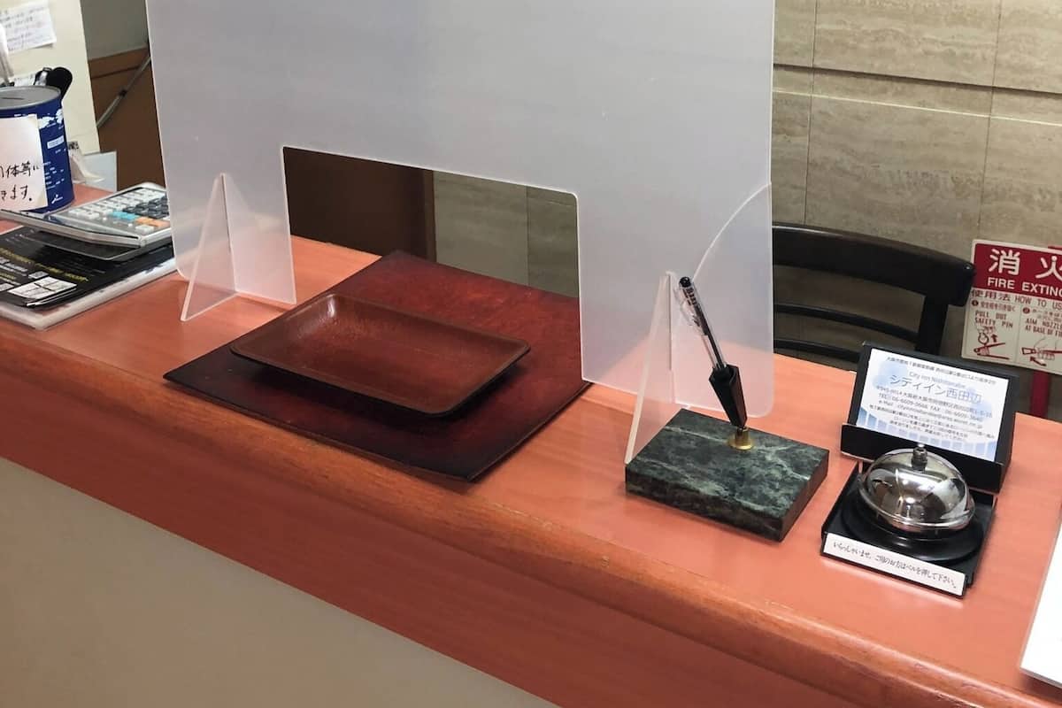 Una mesa de recepción con un monitor de computadora, un portalápices, una pequeña caja y un extintor.