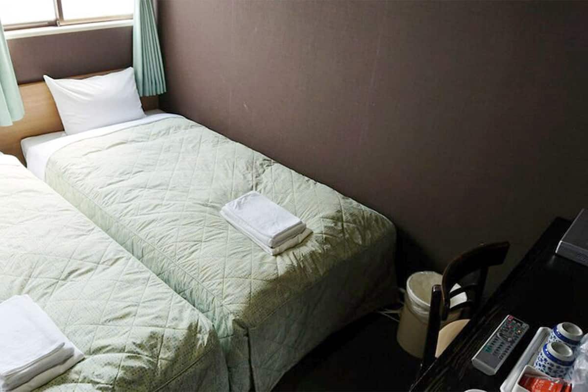 Quarto de hotel com duas camas, uma escrivaninha com um computador e uma cadeira.