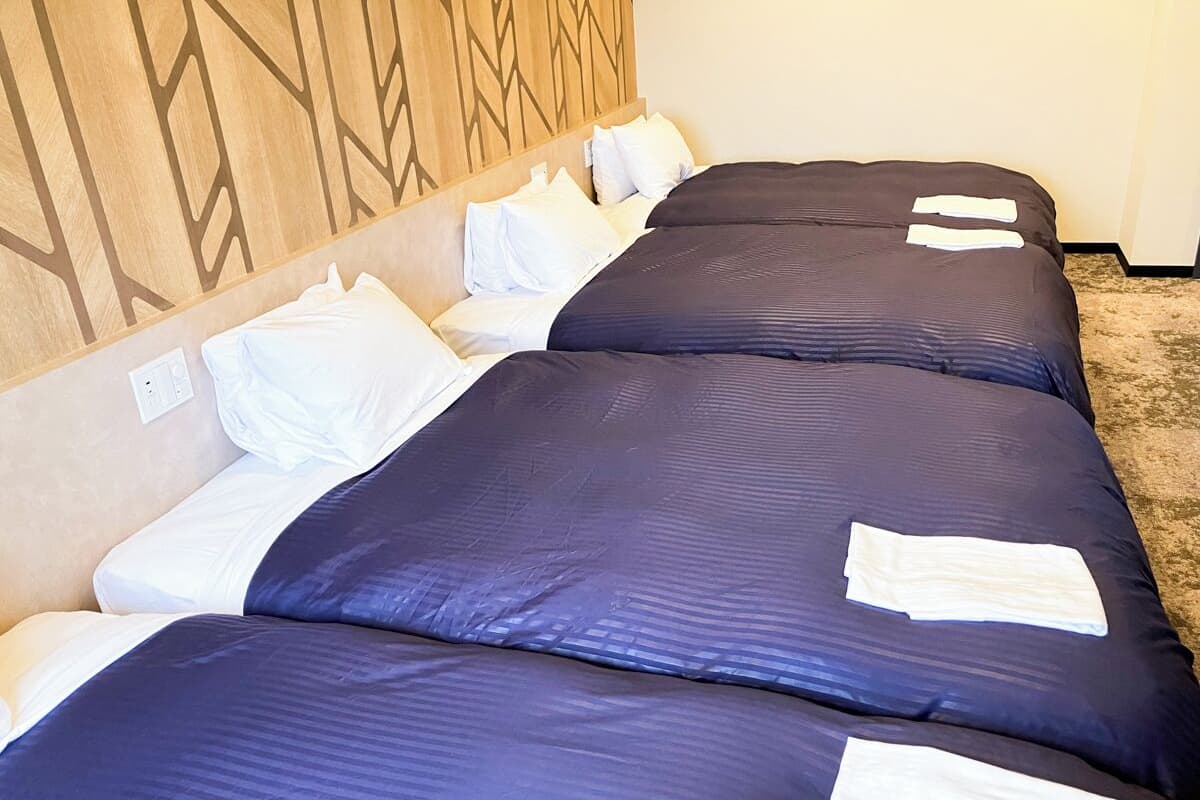 A hotel room with a long bed, white pillows, and a headboard with a geometric pattern.