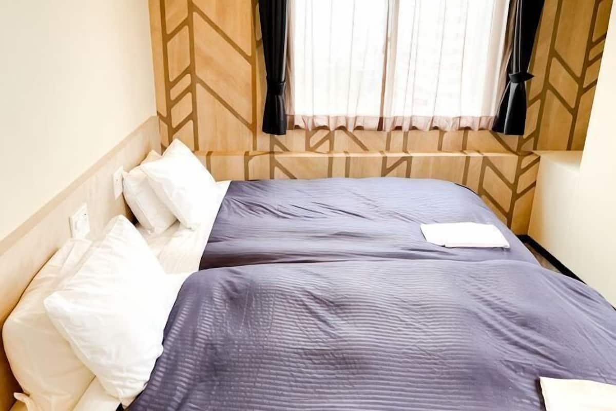 A double bed with white and blue bedding, a wooden headboard, and a window with curtains.