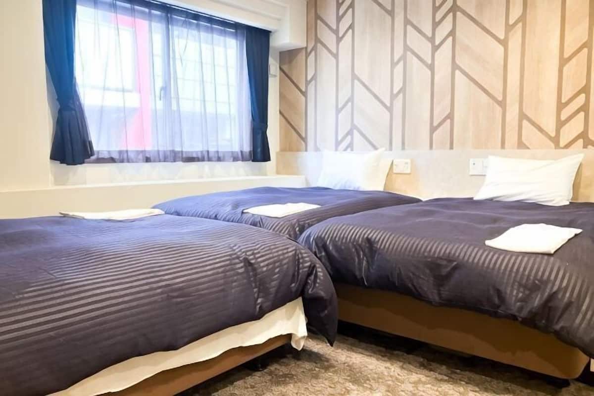 A hotel room with two beds, a window with curtains, and a wooden wall panel.