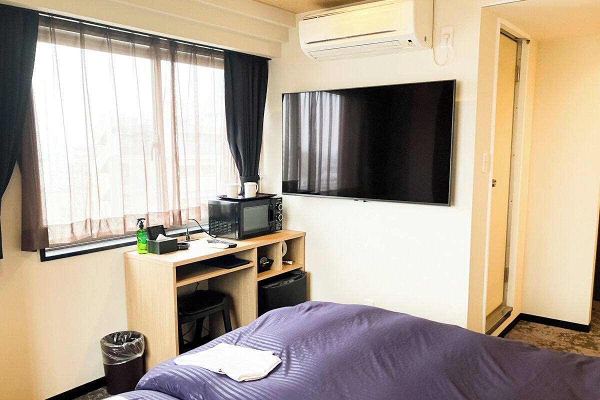 A hotel room with a bed, a desk with a microwave, a TV, and a trash bin.