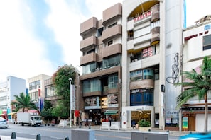 Um edifício com vários andares e diversos estabelecimentos comerciais no térreo, incluindo uma loja visível chamada 'JAZZ'.