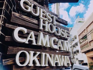 A sign for a guest house named "Camcama Okinawa" with a rustic wooden design.