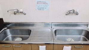 A kitchen sink with two faucets and a note on the wall. - Guesthouse CamCam Okinawa - Hostel (Naha)