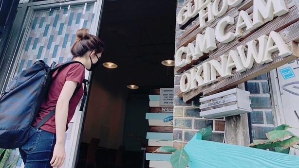 A person entering a building with a sign reading "GUEST HOUSE OKINAWA". - Guesthouse CamCam Okinawa - Hostel (Naha)