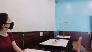 A person seated at a table in a restaurant with a blue wall and wooden paneling. - Guesthouse CamCam Okinawa - Hostel (Naha)
