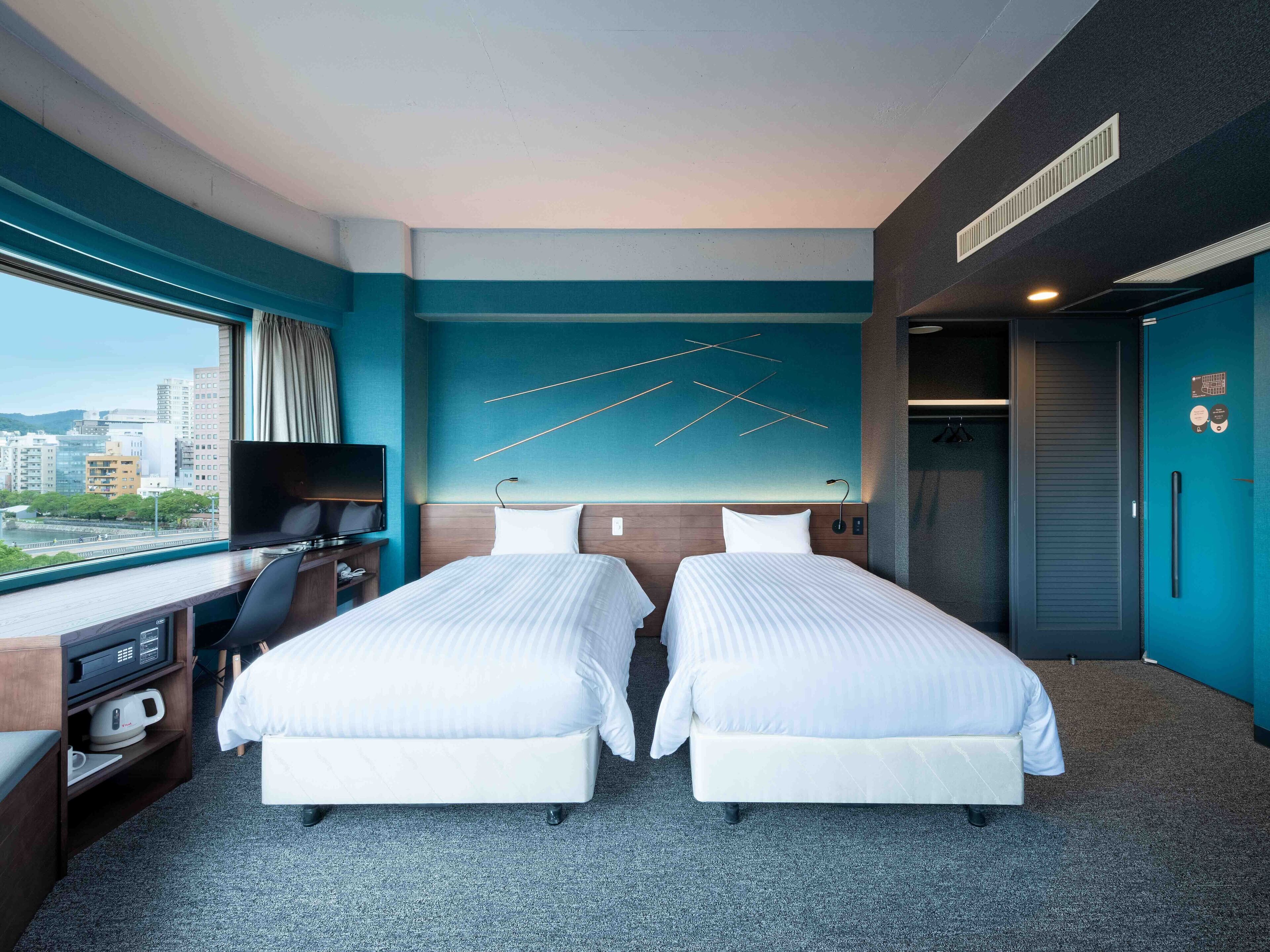 Habitación de hotel con dos camas, un escritorio, un televisor de pantalla plana, vistas a la ciudad y un diseño de pared moderno.