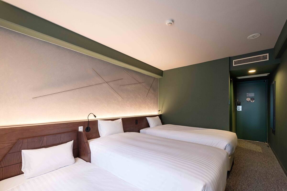 Habitación de hotel con dos camas, una obra de arte grande colocada en la pared, una lámpara en el techo y una puerta con respiradero.