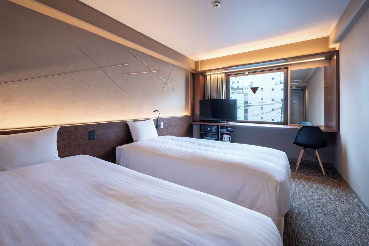 Habitación de hotel con dos camas, televisor, escritorio y ventana con vista a la ciudad.