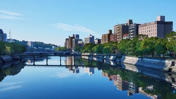 A cityscape with modern buildings, a calm river reflecting the structures, and a clear sky.