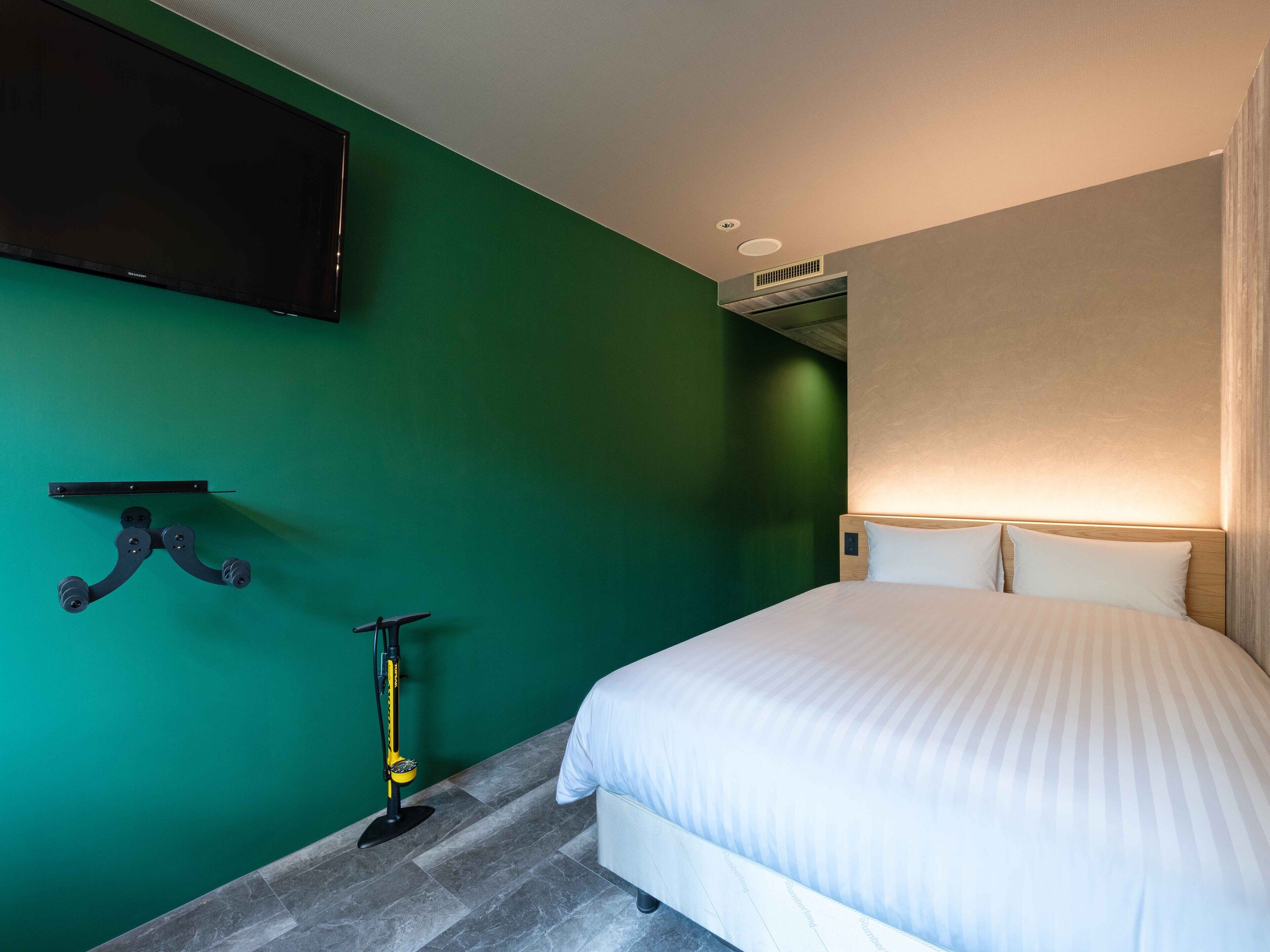 A hotel room with a bed, a mounted television, a scooter, and a wall-mounted air conditioning unit.
