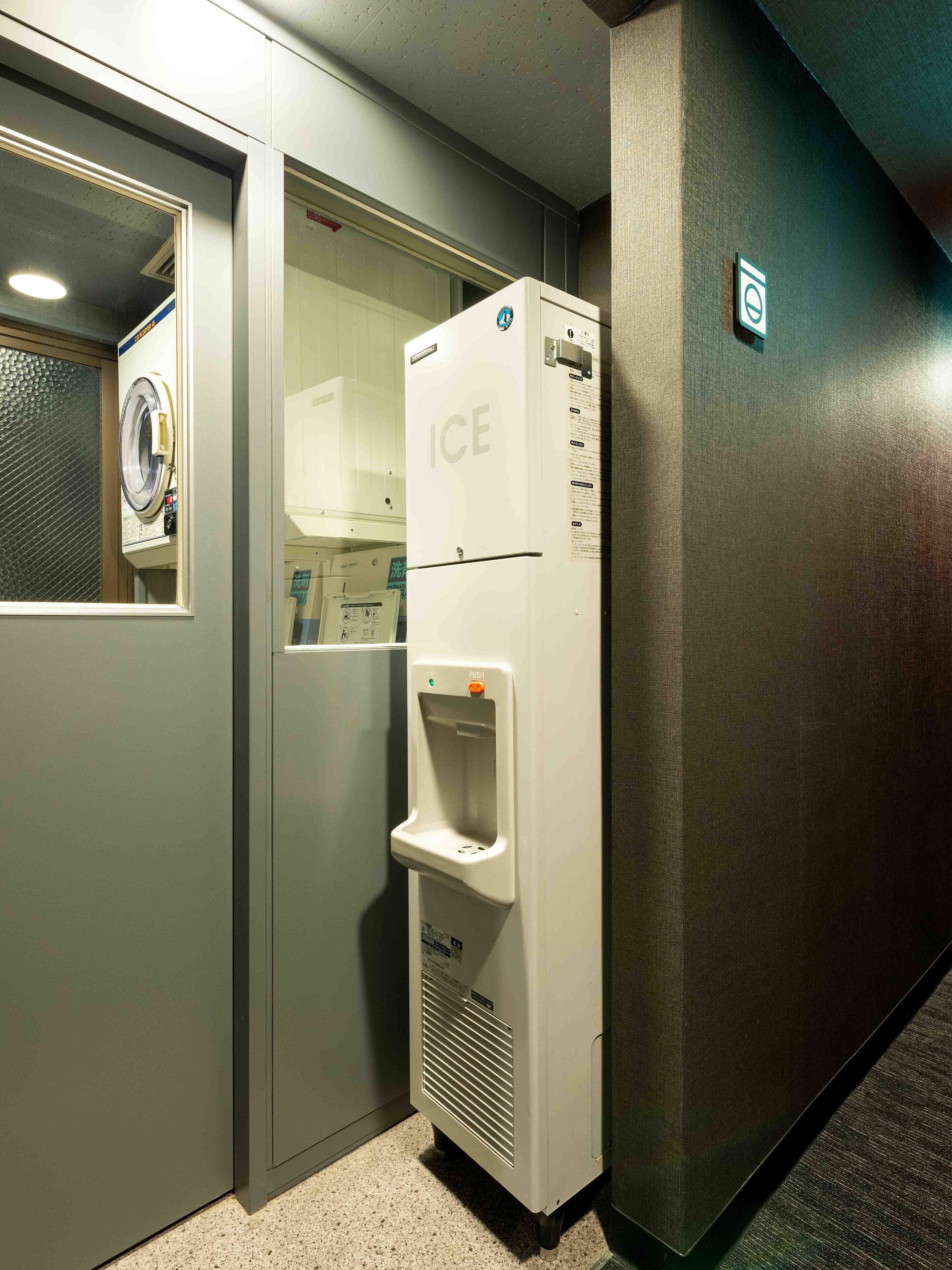 A hotel room with a built-in ice dispenser, a washing machine, and a door with a frosted glass panel.