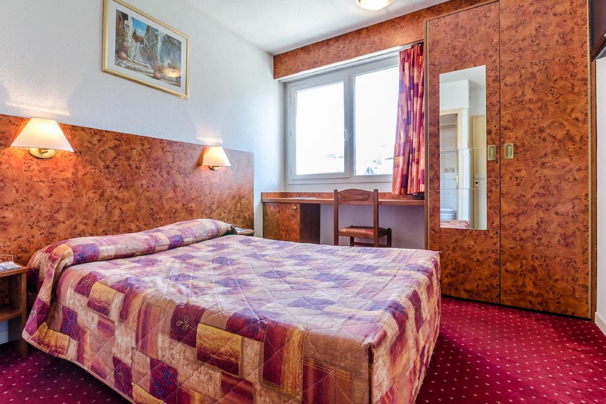 Una habitación de hotel con cama, escritorio, silla y armario.