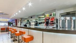 Un área de bar moderna con taburetes naranjas, una barra con grifos de cerveza y una máquina de café a la vista.