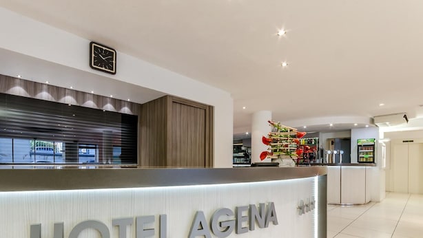Una moderna zona de recepción de hotel con un mostrador curvo, un reloj y un arreglo floral decorativo.