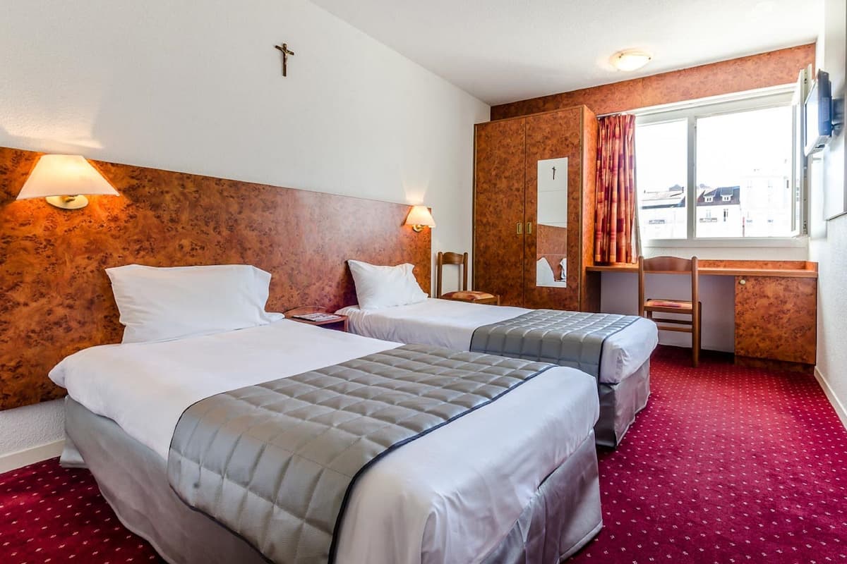 Habitación de hotel con dos camas, un escritorio y una ventana con cortinas.