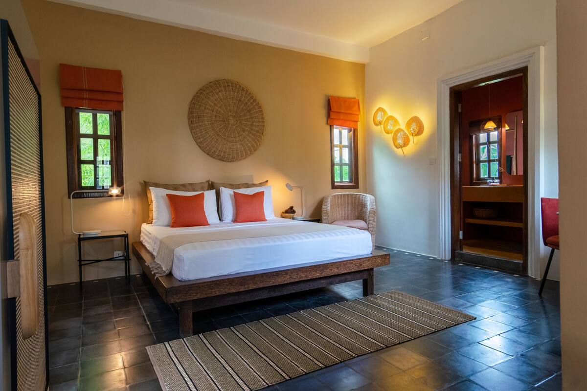 A bedroom with a large bed, two bedside tables, a chair, and a wall-mounted light fixture.