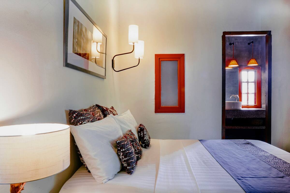A neatly made bed with patterned pillows, a bedside lamp, and a framed artwork on the wall.