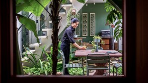 Uma pessoa atendendo uma mesa em um ambiente com escada, paredes verdes e plantas.