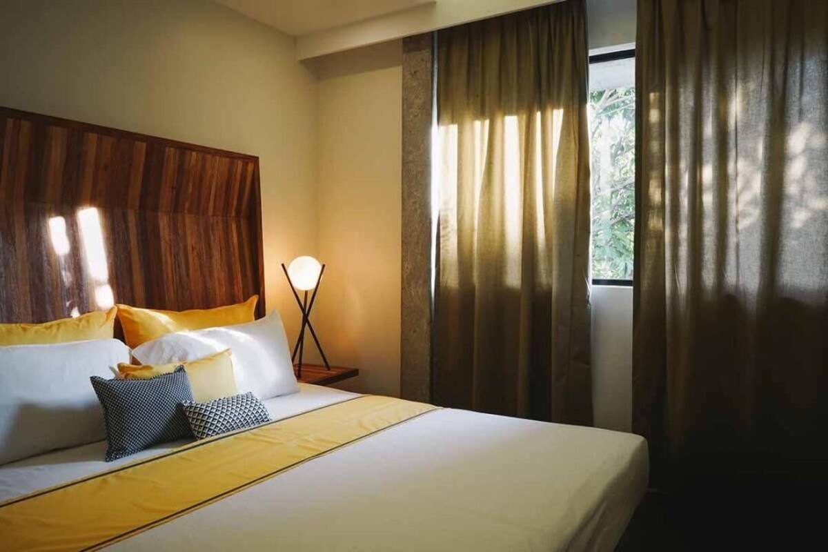 A neatly made bed with a wooden headboard, a bedside lamp, and a window with curtains.