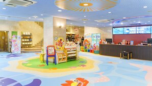 A brightly lit indoor space with a colorful floor design, a reception desk, and a staircase leading to an upper level.