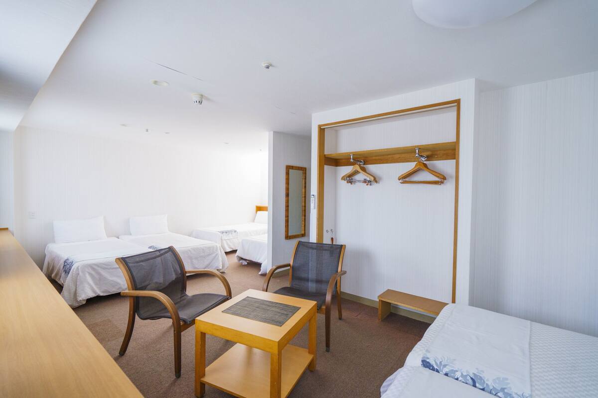 A hotel room with a bed, two chairs, a small table, a coat rack, and a mirror.