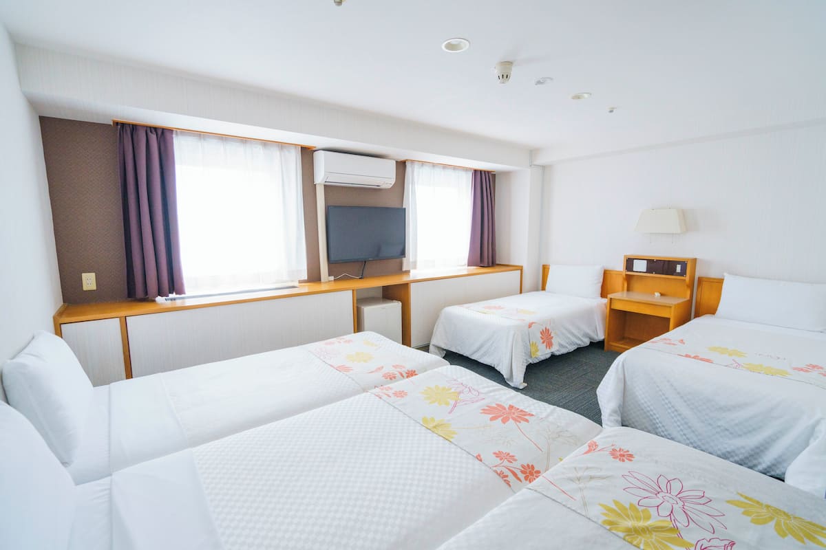 A hotel room with two single beds, a desk with a chair, a television, and a window with curtains.