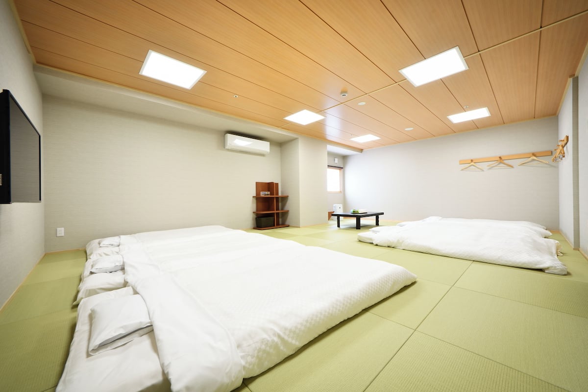 A room with two beds, a small table, and a shelf.