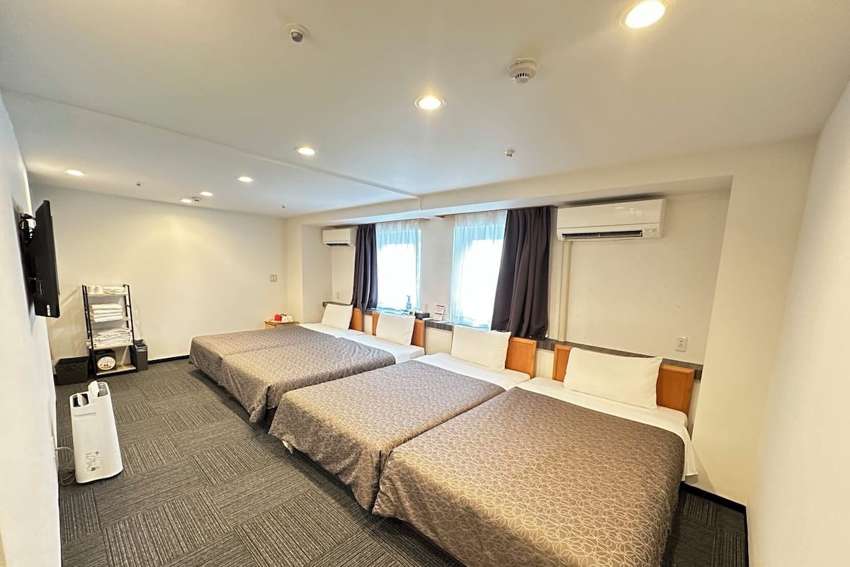 A hotel room with two beds, a TV, a minibar, and an air conditioning unit.