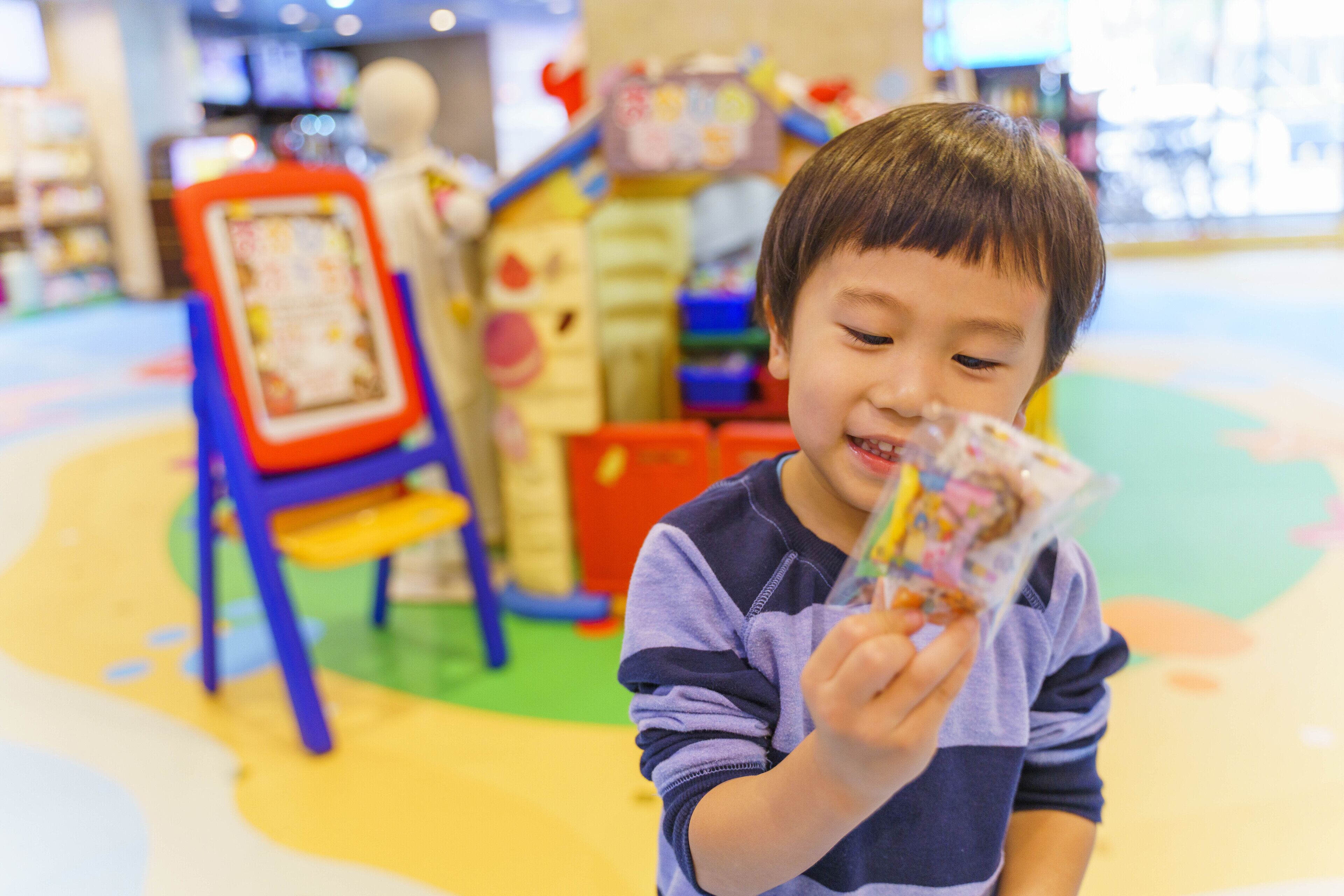 A child holding a toy in a brightly colored indoor play area with various play structures.