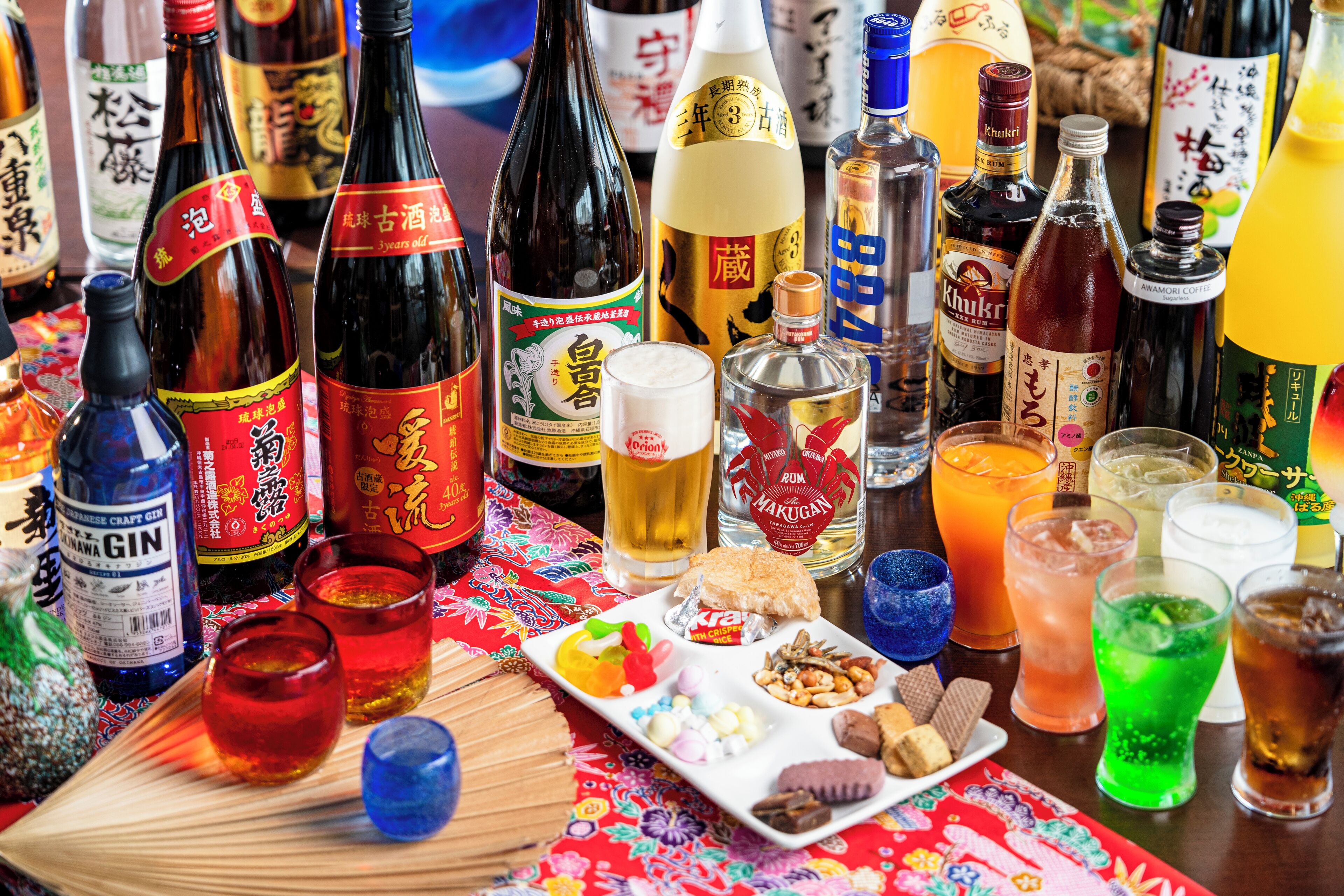 A table with various bottles of alcohol, glasses, and snacks.