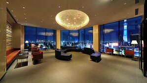 Un hall d’entrée moderne agrémenté d’un grand lustre, de sièges confortables et offrant une vue sur la ville grâce à de larges fenêtres.