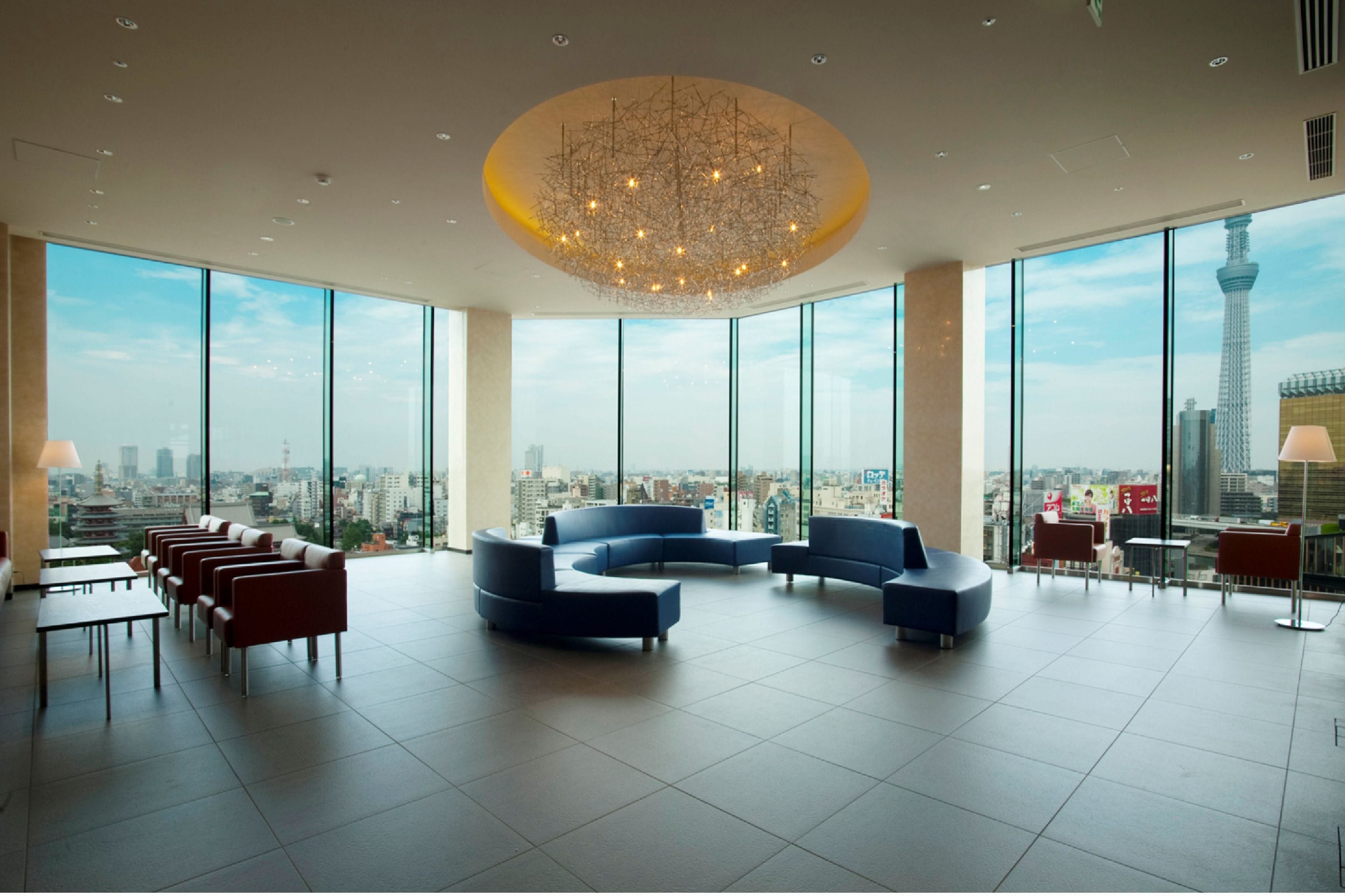 A spacious lounge with a modern chandelier, large windows offering city views, and comfortable seating areas.