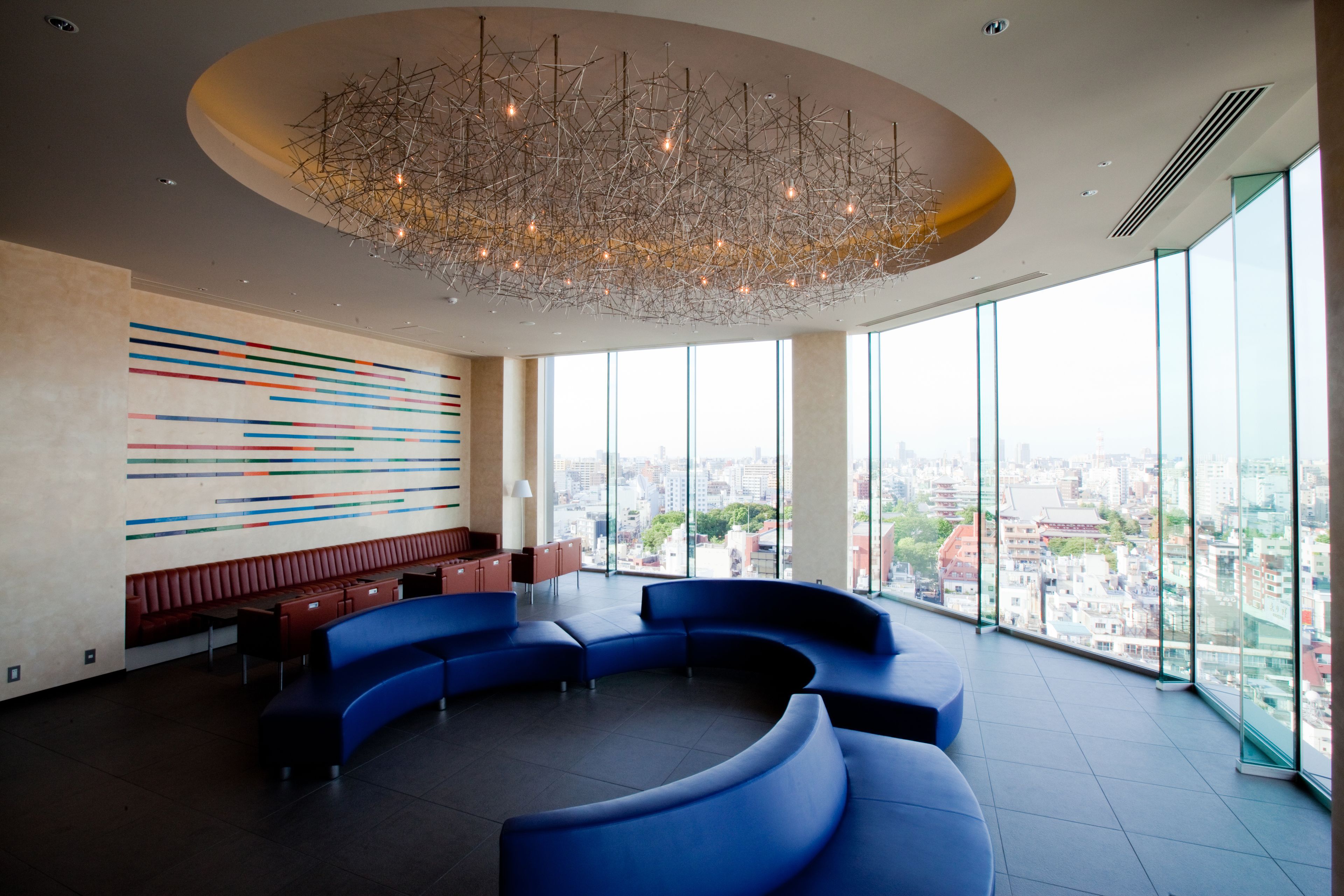 A modern lobby with a curved blue seating area, a colorful abstract wall, and a city view through large windows.