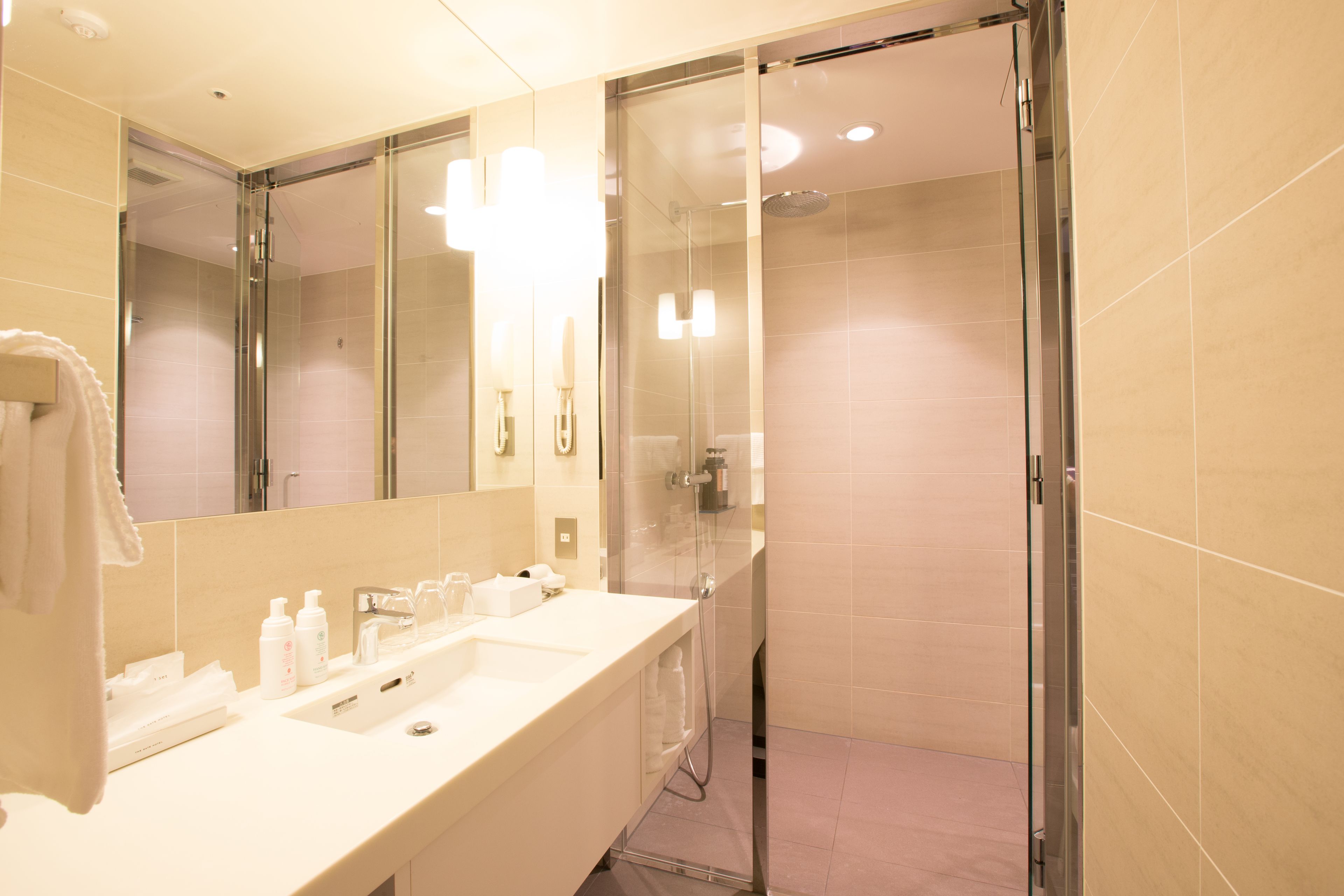 Un baño moderno con ducha de vidrio, un espejo grande y un lavamanos blanco con artículos de aseo.