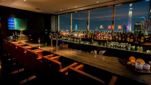Un bar offrant une vue sur les toits de la ville, avec des tabourets et une grande variété de bouteilles et de verres.