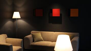 A dimly lit room with a sofa and two armchairs, a floor lamp, and three wall-mounted square light panels.