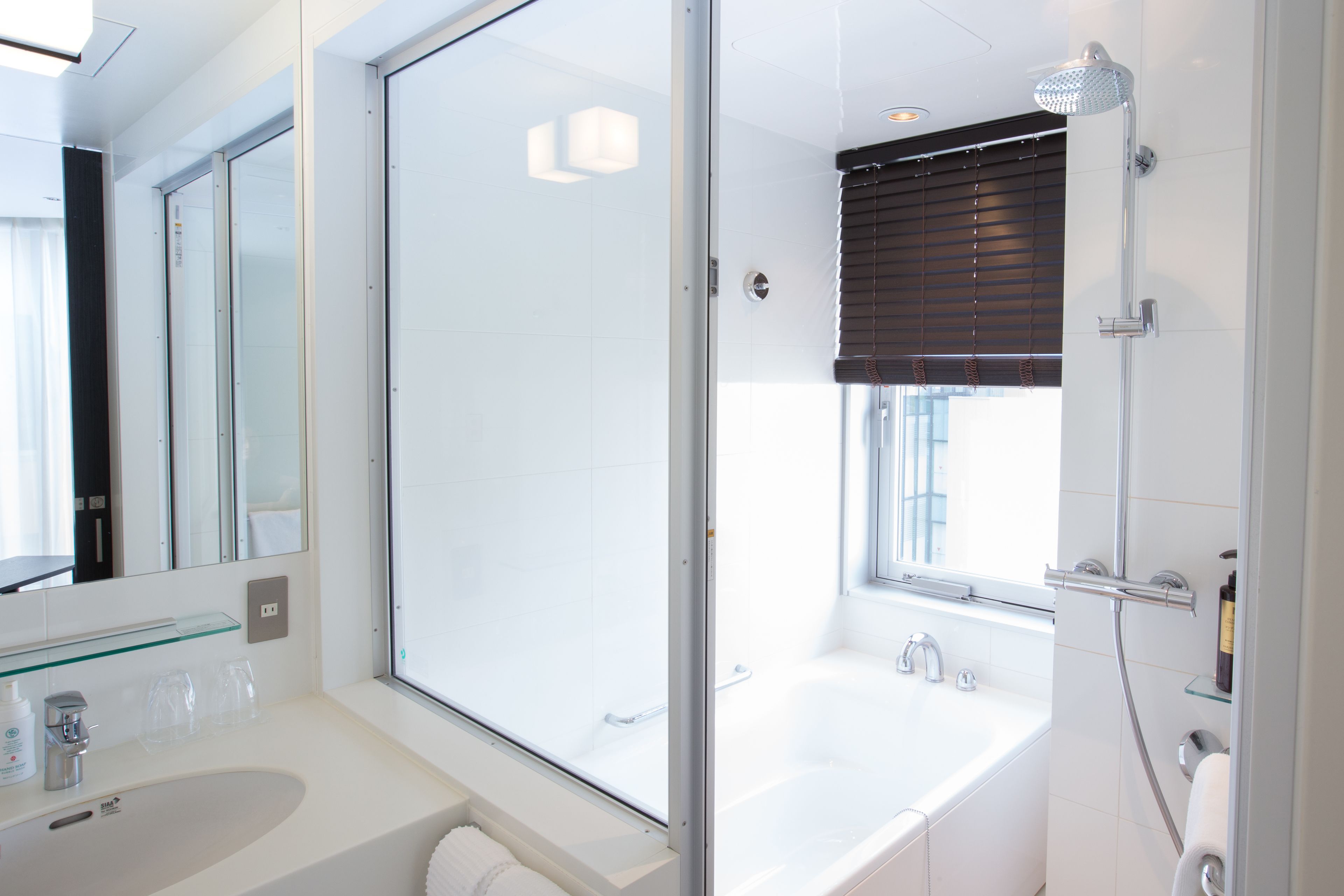 A modern bathroom with a glass shower enclosure, a standalone bathtub, and a glass-topped vanity.