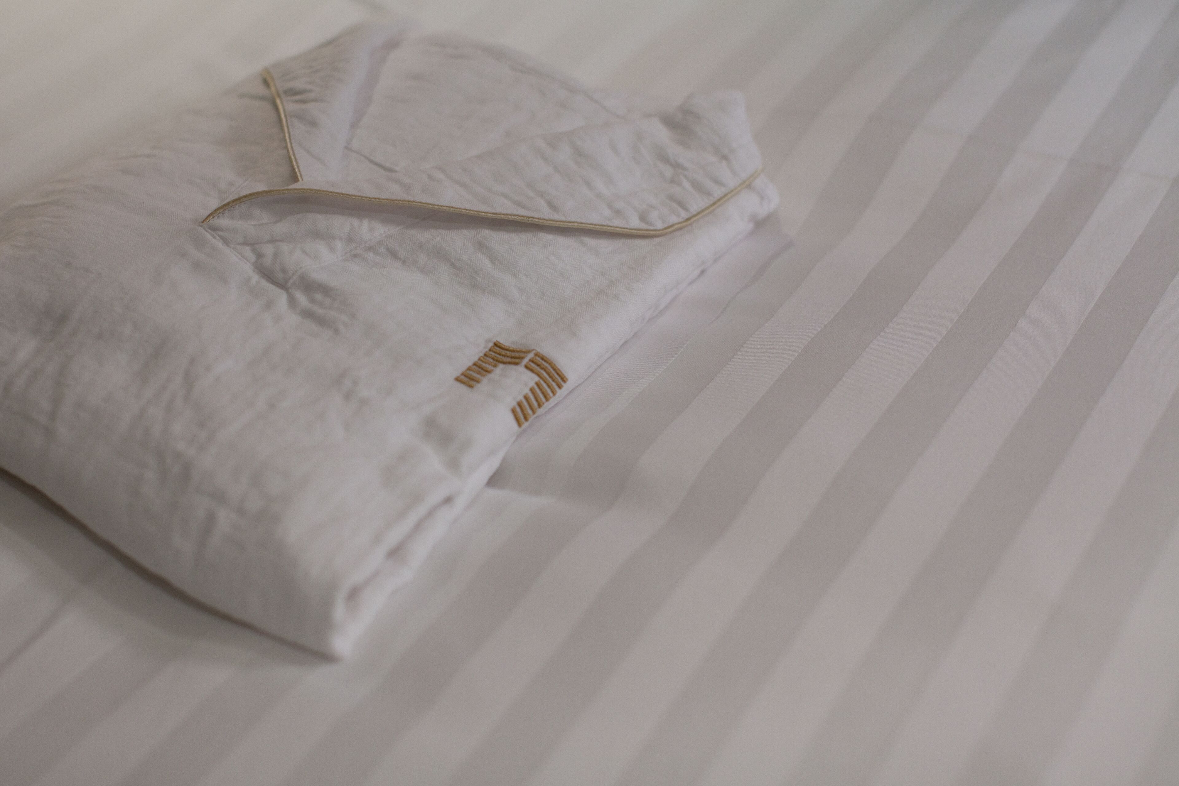 Almohada blanca doblada con detalle dorado sobre un edredón a rayas.