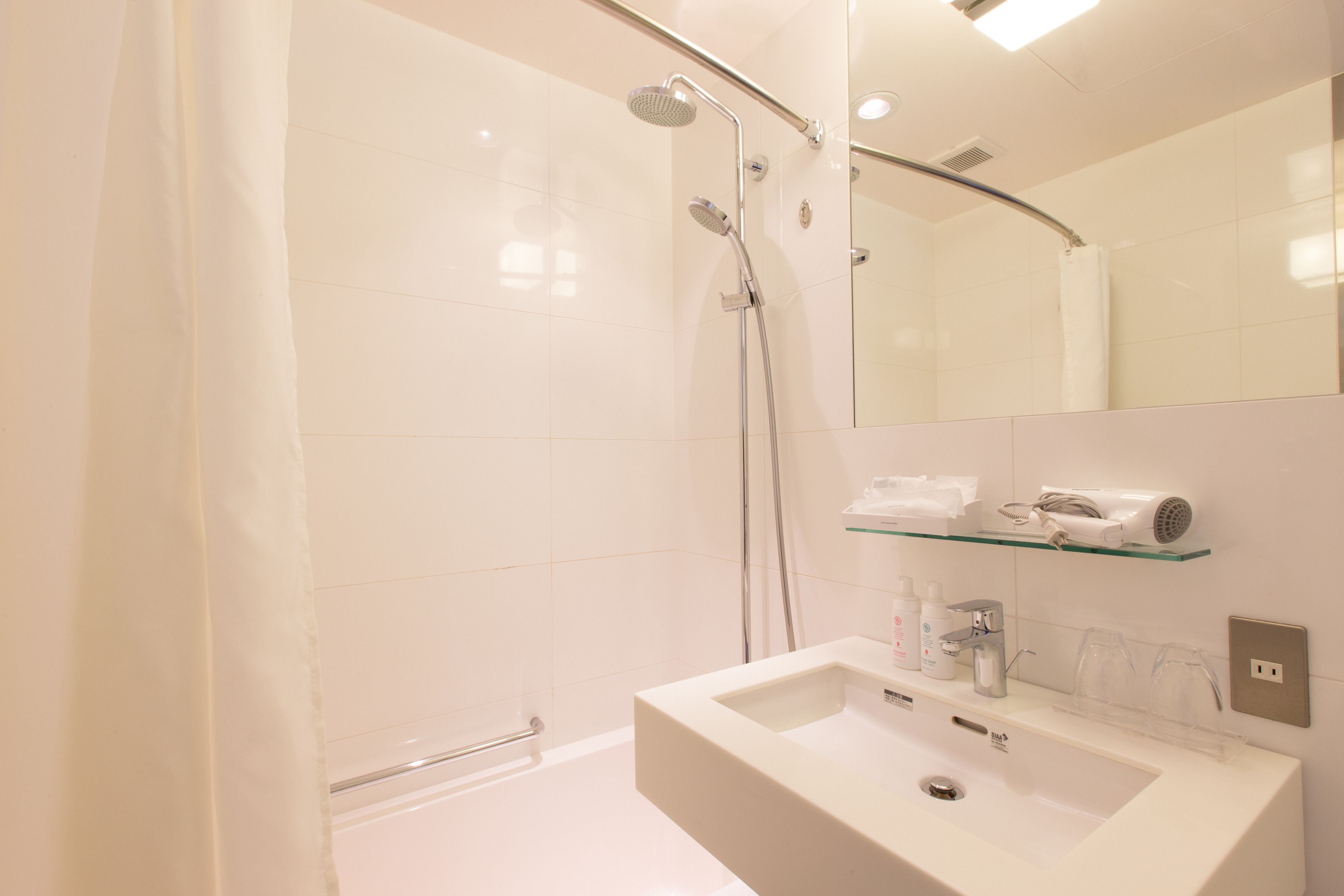 A modern bathroom with a shower, a sink, and a glass shelf with toiletries.
