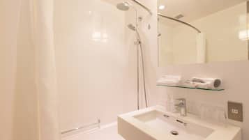 A modern bathroom with a shower, a sink, and a glass shelf with toiletries.